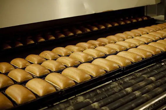 "Panecillos recién horneados en bandejas dentro de la línea de producción industrial de La Lorraine, cuyo rendimiento es monitorizado por el sistema MES."