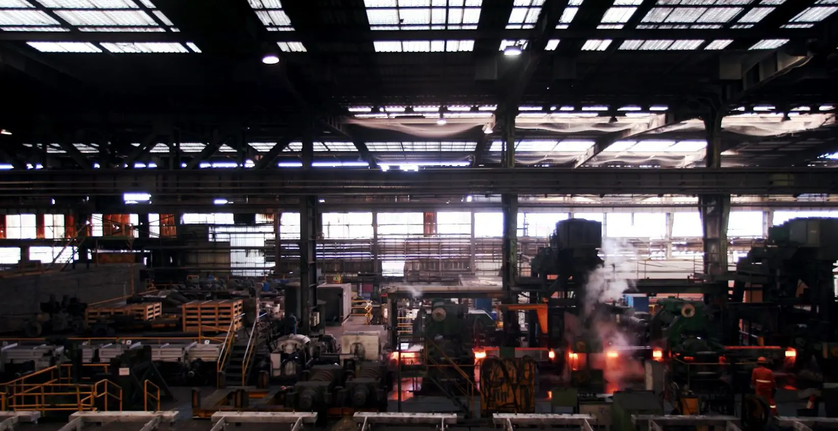 "Vista interior de la planta metalúrgica de CELSA, mostrando un entorno industrial a gran escala con maquinaria, estructuras elevadas, vapor y zonas de almacenamiento de material."