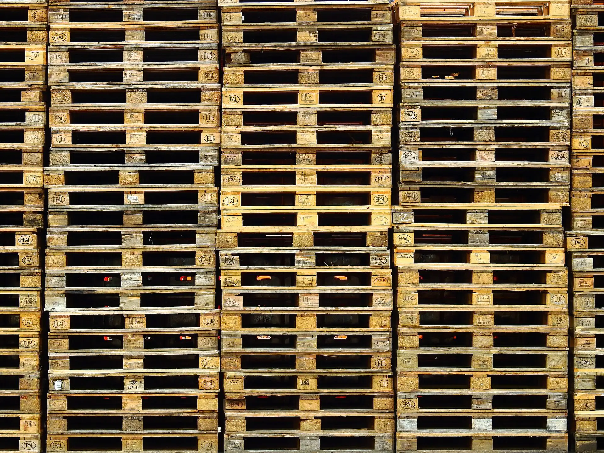 "Pared de palets de madera tipo EUR apilados de forma ordenada, representando la alta capacidad de producción y el stock de producto terminado de la fábrica de ATM Pallets."