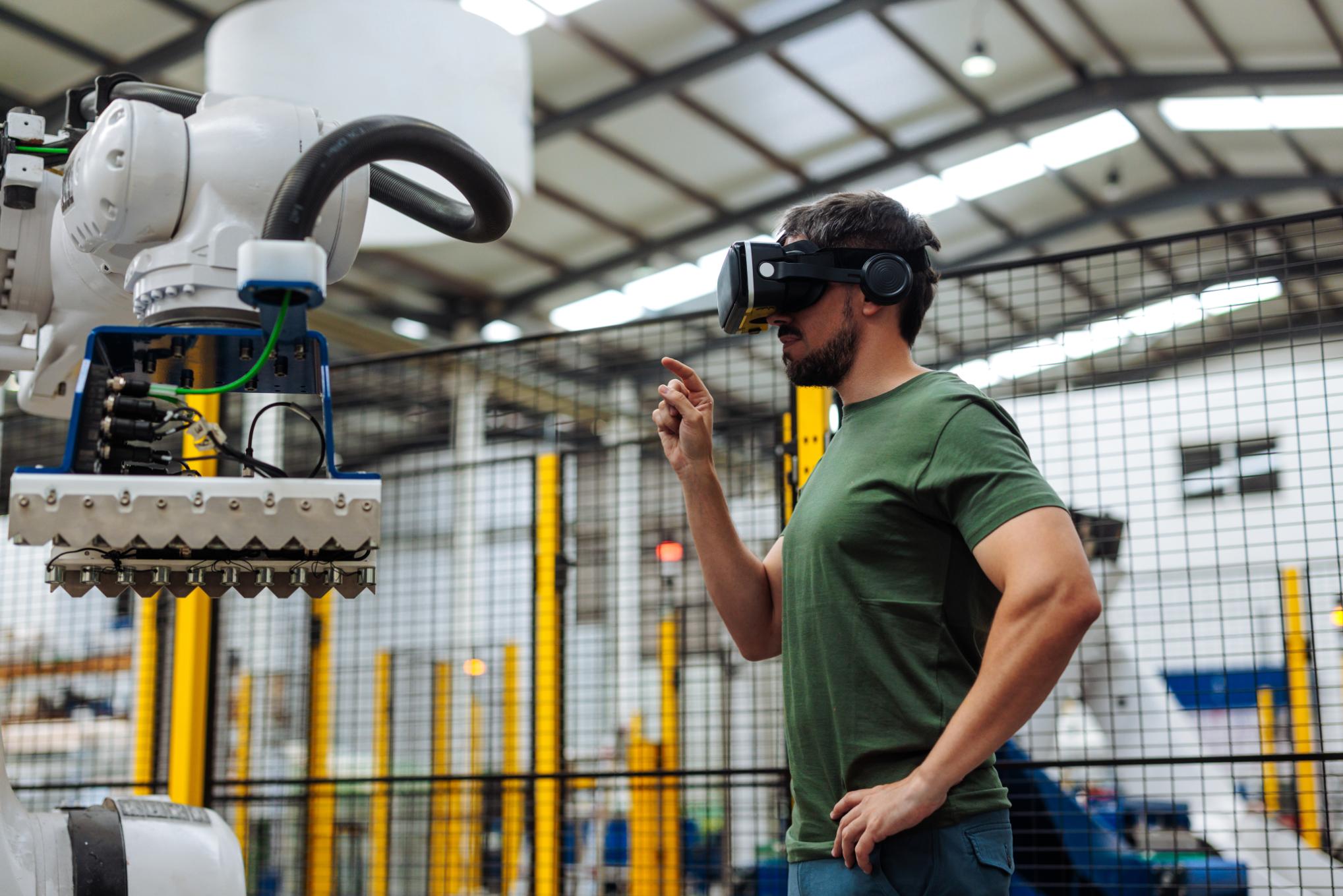 Operario usando gafas de realidad aumentada y virtual para interactuar con un robot industrial en una fábrica.